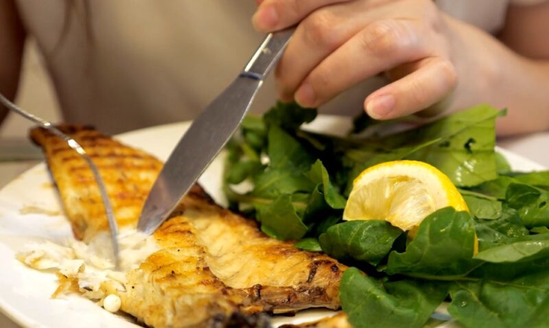 A person cutting a fish with a fork