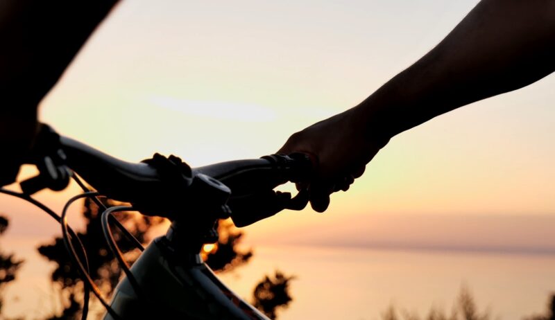 Human hands holding bike brakes with sunset in the background