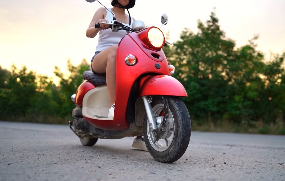 A girl rides red moped