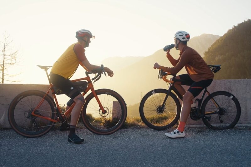 Two bikers are taking a rest from cycling, drinking water in the sunset