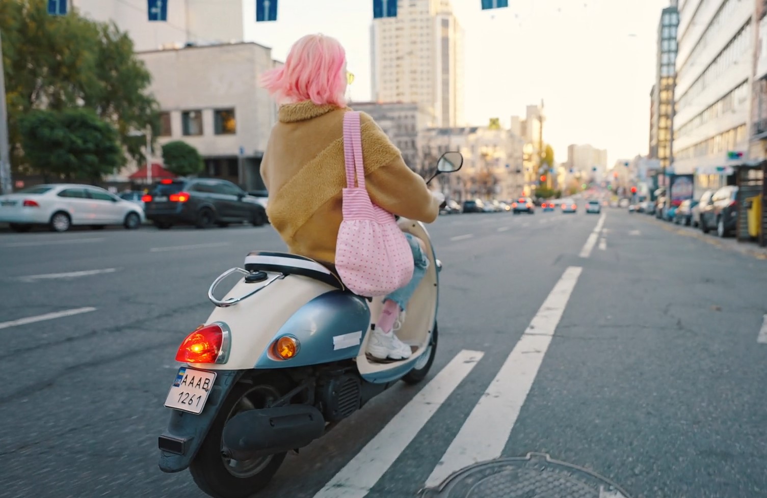 Girl with pink hair rides a moped in a city