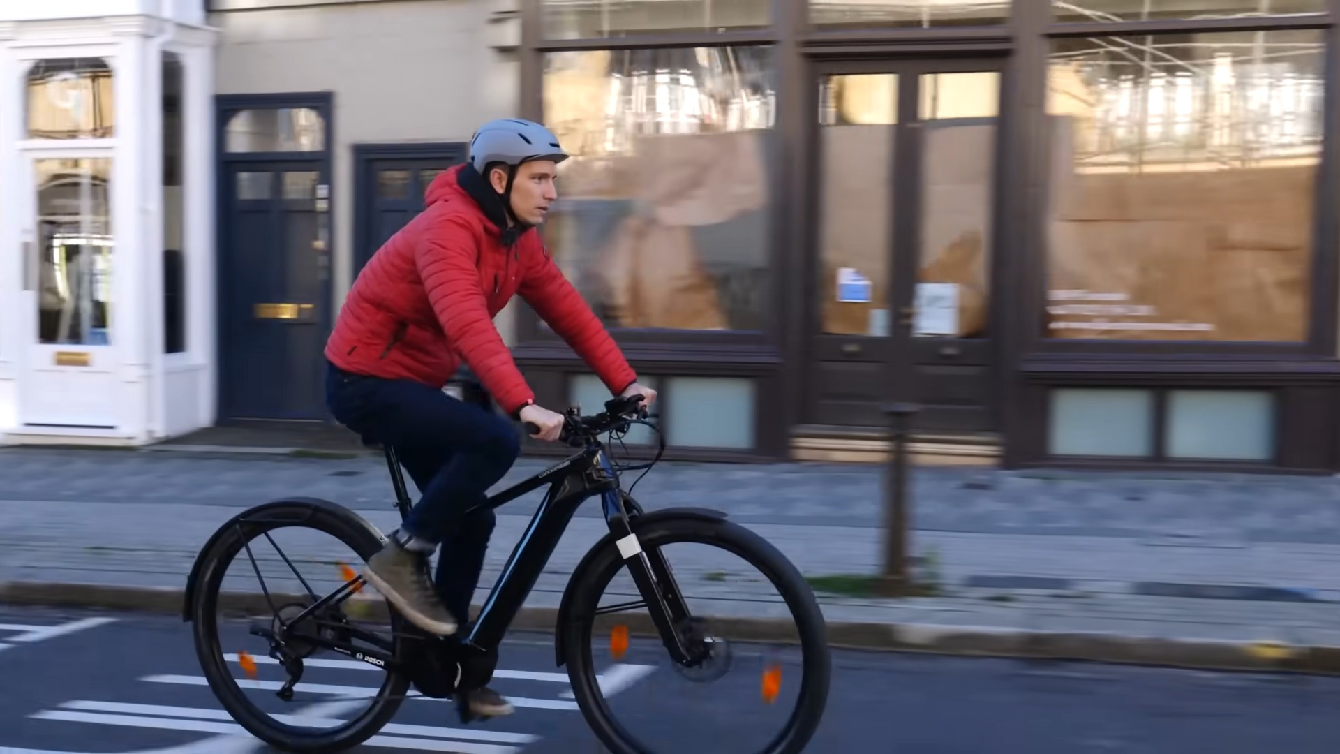 A guy in a red jacket rides e-bike, wearing helmet