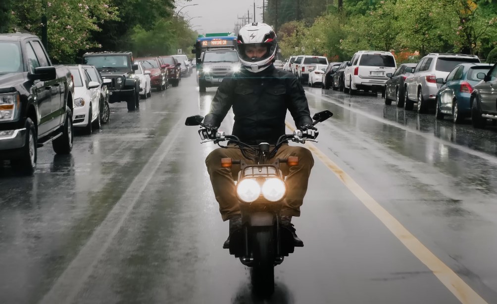 A guy with a helmet rides a moped on a rainy road