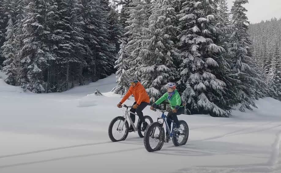 A guy and a girl riding fat bikes on a snowy road