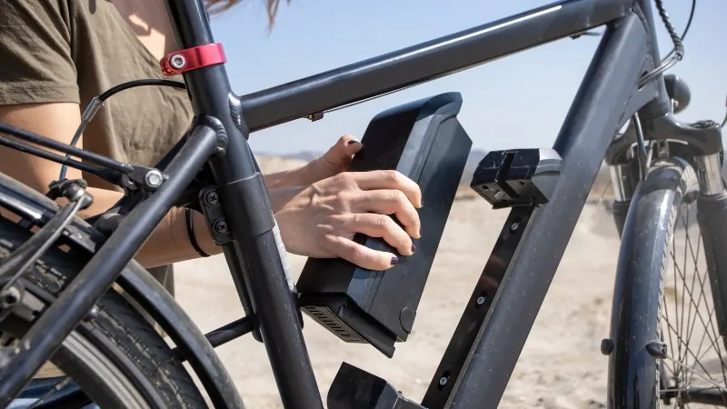 A person removes the battery from an e-bike, checking for common electric bike problems during outdoor maintenance