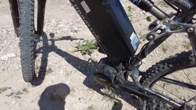 Close-up of an electric bike motor and battery system on a dirt trail, showing the wiring and mid-drive unit