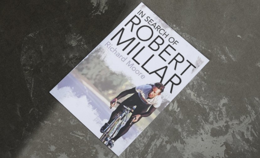 A book cover, "In Search of Robert Millar," by Richard Moore, rests on a textured surface