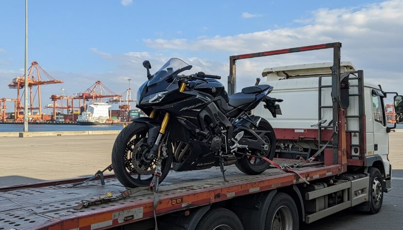 A motorcycle is being loaded onto a flatbed truck by a person using a ramp