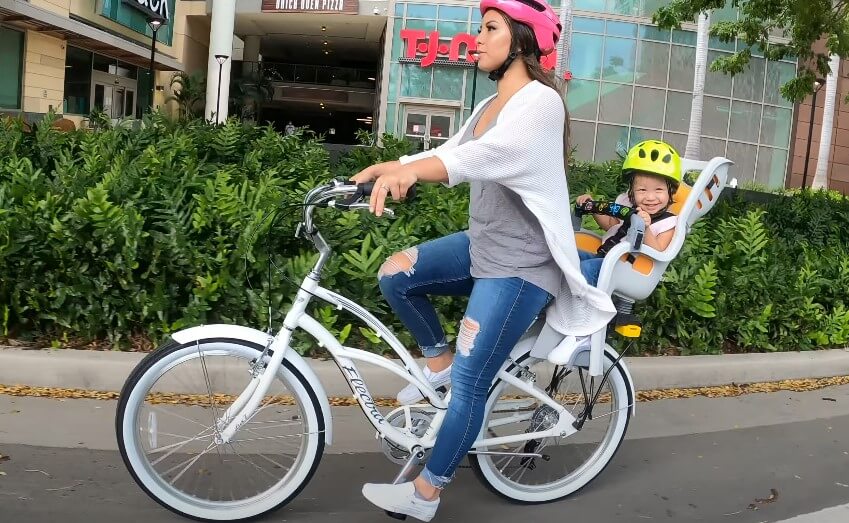 A woman rides a bicycle with a child securely seated in a child seat behind her