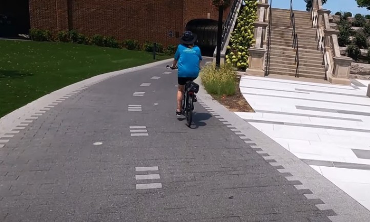  A person cycling along a smooth, paved path surrounded by greenery
