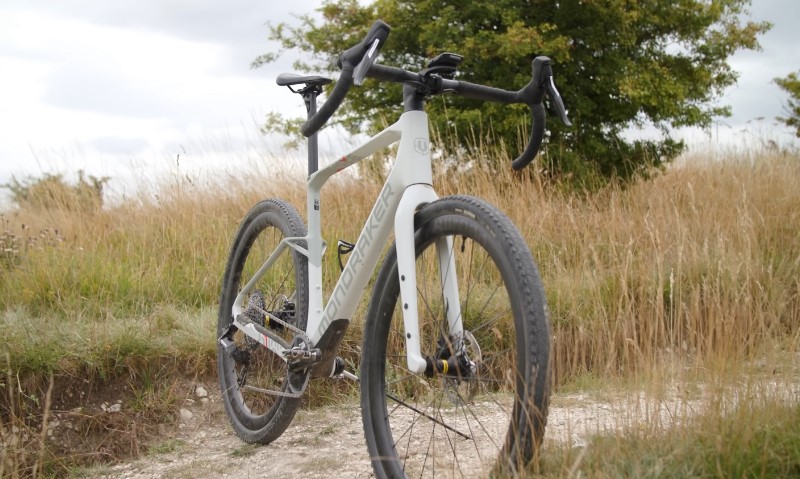 White gravel bike with drop handlebars parked on a dirt path amidst tall