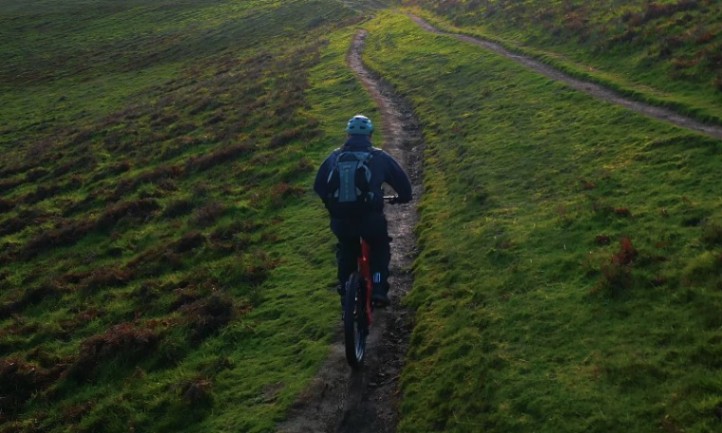 A person riding a mountain bike along a dirt trail surrounded by trees and rocky terrain