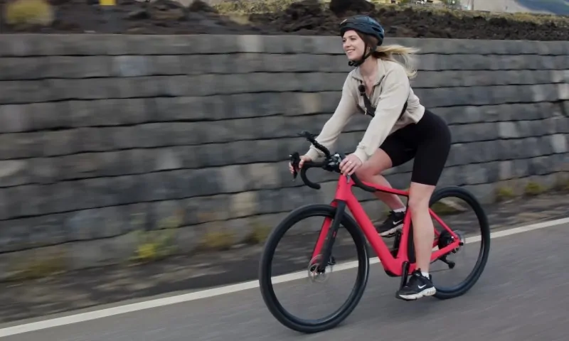 A woman rides a pink bike along a road, enjoying a sunny day outdoors