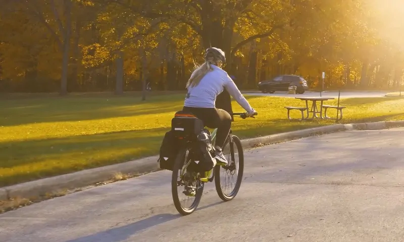 A woman riding a bicycle on a paved road, surrounded by greenery and a clear blue sky