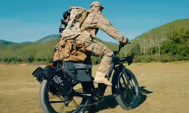 A soldier riding a Fiido Titan bike through a wide, open field under a clear blue sky