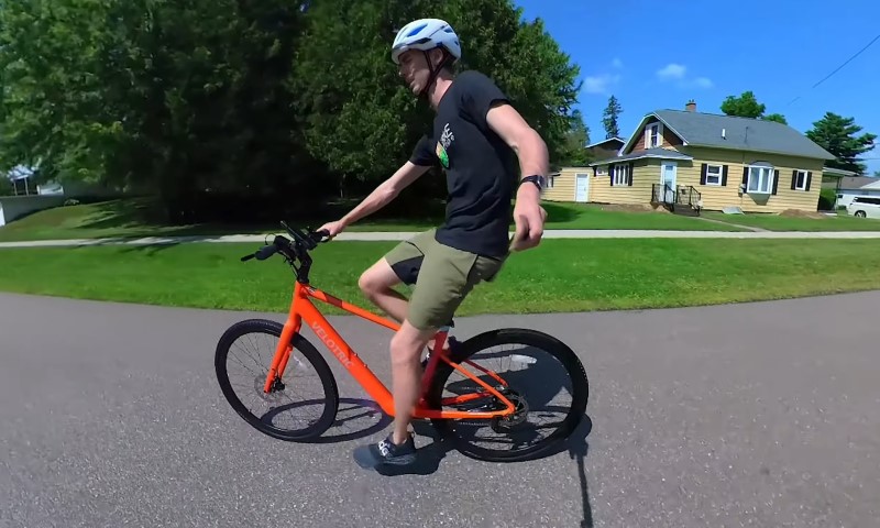 A man rides an orange bike along a street
