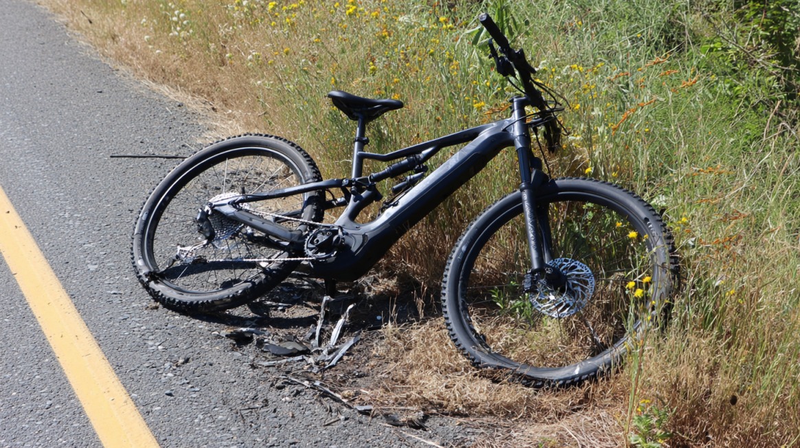 A damaged electric bike lying off the road near tall grass