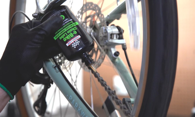 A person wearing black gloves applies lubricant to a bicycle chain