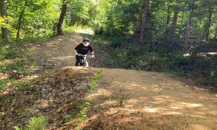 A person wearing a helmet rides a bike on a forested dirt trail