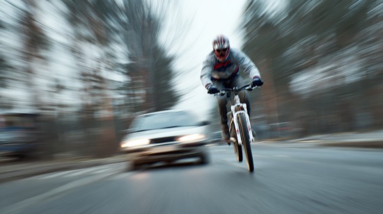Blurred motion shot of a cyclist riding fast on a public road with a car approaching behind