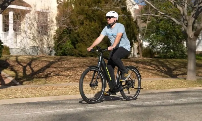 A person wearing a helmet rides a black electric bicycle on a sunny street