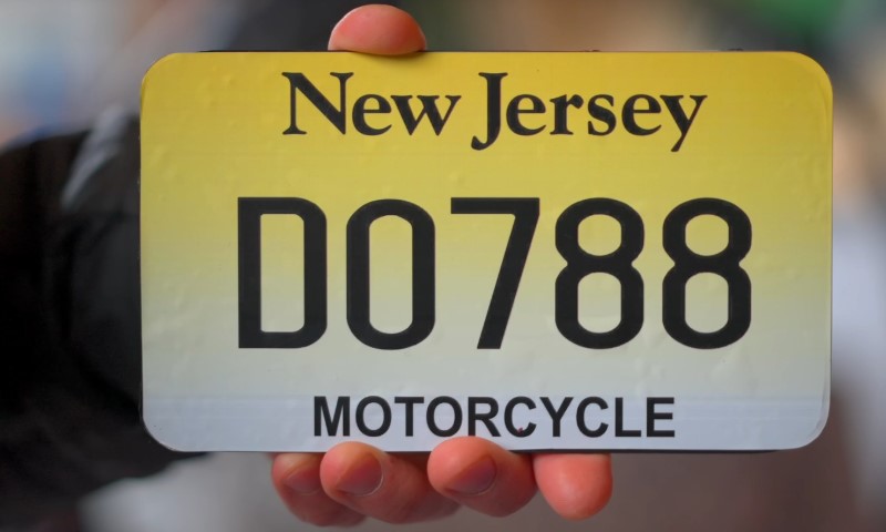 A hand holds a New Jersey motorcycle license plate with the number D0788