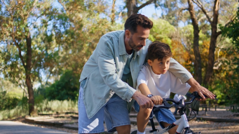 Parent guiding a child learning to ride an electric bike in a park setting