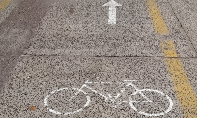 Paved road with a white bicycle symbol and an arrow pointing ahead, indicating a bike lane