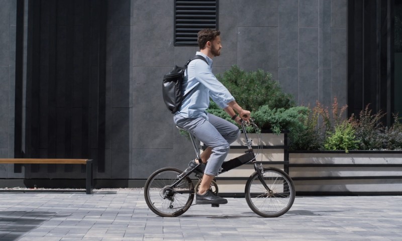 A man in a blue shirt and gray pants rides a folding bike on a paved area