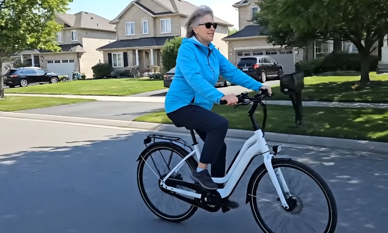 A person in a bright blue jacket rides a white bicycle down a suburban street