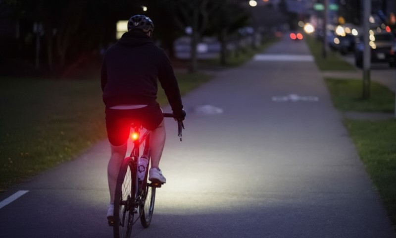 A cyclist wearing a helmet and dark clothing rides on a dimly lit path at dusk